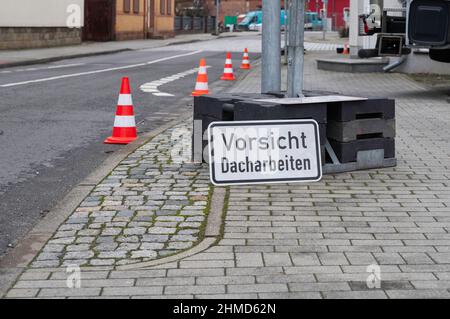 Ein Schild mit der deutschen Aufschrift Vorsicht Dacharbeiten Stockfoto