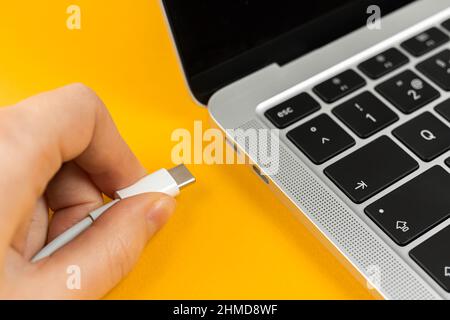 Frau, die ein Ladegerät in einen Laptop einsteckt. Ladeanschluss Typ C. Konzept für niedrigen Batteriestand Stockfoto