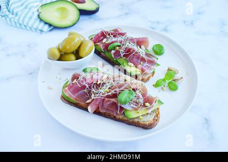 Vollkornbrot-Sandwiches mit Scheiben Avocado, Prosciutto oder Jamon, gekeimten Samen und Kräutern. Sauberes Essen, gesundes Frühstück. Draufsicht Stockfoto