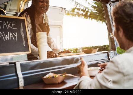 African Senior Woman Serving Take Away Food inside Food Truck - Focus on Cutting Board Stockfoto