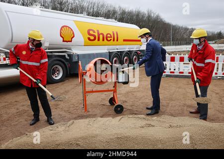 09. Februar 2022, Nordrhein-Westfalen, Köln: Hendrik Wüst (M, CDU), Ministerpräsident von Nordrhein-Westfalen, Fabian Ziegler (l), Geschäftsführer von Shell in Deutschland, Und Marco Richrath (r), General Manager des Energie- und Chemieparks Rheinland, schaufelt Sand beim Baubeginn einer CO2-neutralen bio-flüssigen Erdgasanlage (Bio-LNG) auf dem Raffineriestandort Shell. Die Anlage wird voraussichtlich ab Mitte 2023 rund 100.000 Tonnen Bio-LNG pro Jahr für den Schwerlasttransport produzieren. Foto: Oliver Berg/dpa Stockfoto