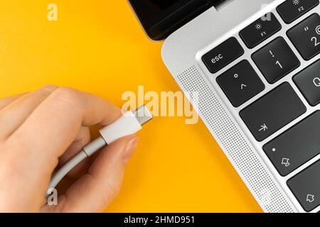 Frau, die ein Ladegerät in einen Laptop einsteckt. Ladeanschluss Typ C. Konzept für niedrigen Batteriestand Stockfoto