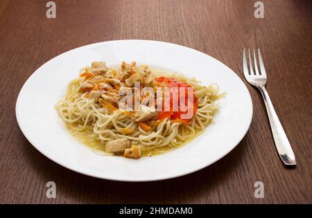 Spaghetti mit Fleisch und Gemüse auf einem weißen Teller auf einem Holztisch. Nahaufnahme im Innenbereich Stockfoto