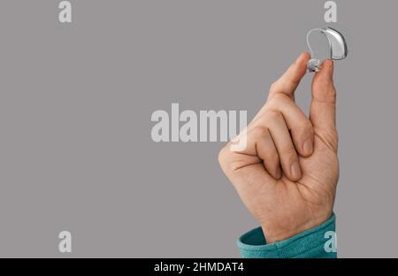 Hörgerät in männlicher Hand, Nahaufnahme auf grauem Hintergrund mit Platz für Text. Hörlösungen, BTE-Hörgeräte Stockfoto