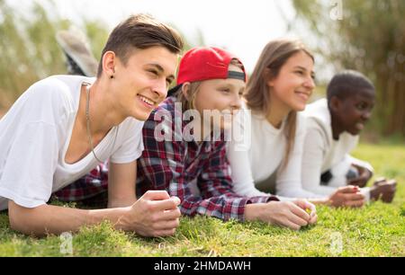 Multinationale moderne Teenager liegen im Park auf dem Rasen Stockfoto