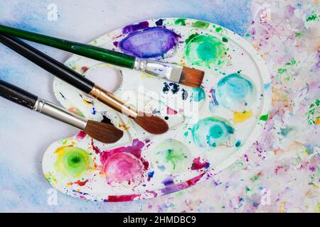 Nahaufnahme der Kunstpalette mit Flecken, Pinsel, Papier mit bunten Aquarellzeichnungen. Konzept Hobby, Handwerk, Kreativität Stockfoto