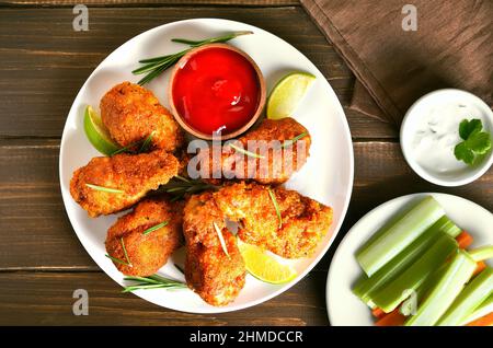 Gegrillte Hähnchenflügel und Tomatensoße auf weißem Teller auf Holzhintergrund. Draufsicht, flach liegend Stockfoto