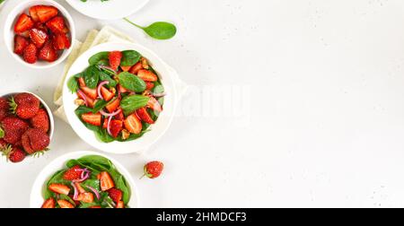 Obstsalat mit Erdbeere, Spinat und Walnuss auf hellem Hintergrund mit Kopierfläche. Frische Erdbeeren Scheiben in Schüssel. Draufsicht, flach liegend. Stockfoto