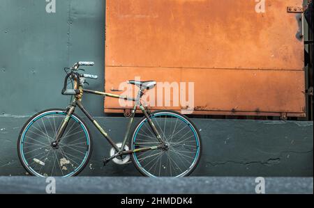 Ein Fahrrad vor einer orangefarbenen Stahltür mit einer grünen Lagerhauswand. Kopierbereich, selektiver Fokus. Stockfoto