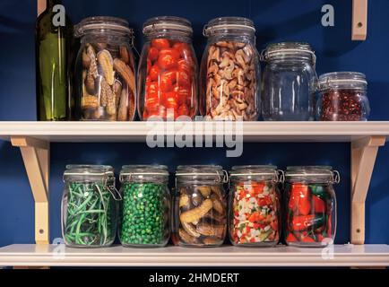 Glasgefäße mit eingelegtem und gesalzenem Gemüse auf einem Regal im Kücheninnenraum. Hausgemachte Speisen. Stockfoto