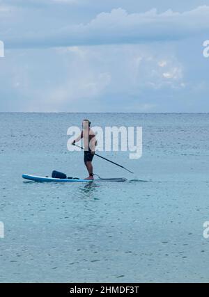 Ein sportlicher junger Mann schwebt mit einem Paddel in der Hand am Strand in Playa del Carmen, Mexiko Stockfoto