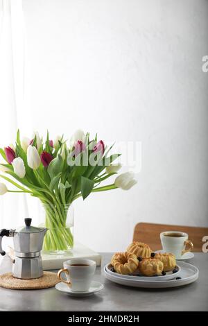 Mini-Bunt-Kuchen mit Früchten auf dem Teller, einer Tasse Kaffee und einem Bouquet von Tulpen. Stockfoto