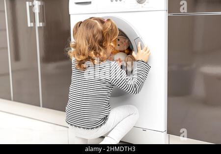 Das Kind beobachtet, wie die Waschmaschine waschen wird. Stockfoto