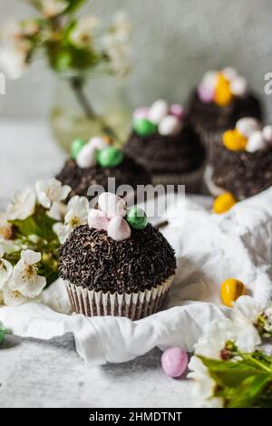 Hausgemachte Oster-Schokolade-Cupcakes mit Schokoladenbutter-Creme-Zuckerguss und Süßigkeiten-Eiern. Osterbrunch. Frühlingsblumen-Dekoration. Auf weißem Leinentisch Stockfoto