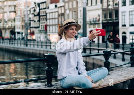 Fröhliche Frau, die während der Reise Selfie auf der Bank nimmt Stockfoto