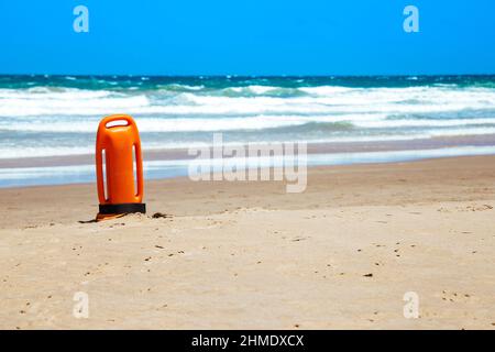 Rettungsschwimmer kann am Strand. Orangefarbene Rettungsboje in vertikaler Position auf dem Sand. Stockfoto