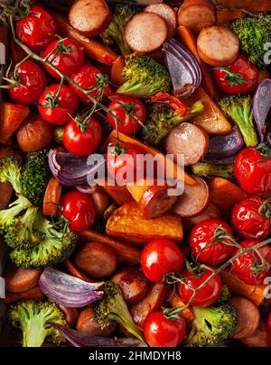 Im Ofen gebackenes Gemüse und Würstchen, gesundes Mittagessen, Süßkartoffel Zwiebel Tomate Brokkoli Stockfoto