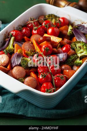 Im Ofen gebackenes Gemüse und Würstchen, gesundes Mittagessen, Süßkartoffel Zwiebel Tomate Brokkoli Stockfoto