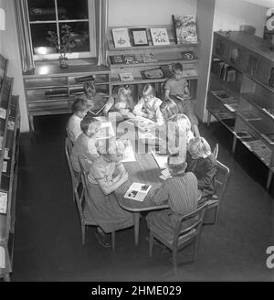 Kinder von 1950s Jahren. Das Innere einer öffentlichen Bibliothek und ein Raum mit Bücherregalen an den Wänden. Eine Gruppe von Kindern sitzt an einem Tisch und liest jeweils ein Buch. Schweden 1951 Kristoffersson Ref. BE25-12 Stockfoto