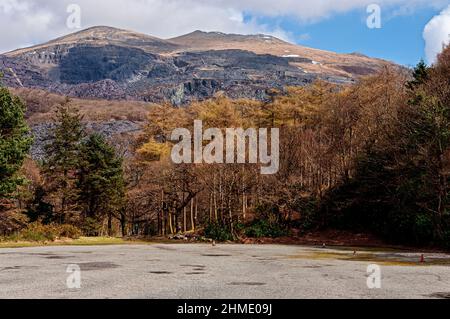 Die freiliegende graue Tiernarbe aus einstürzenden riesigen Stufen und Gebäuden, die Überreste einer stillgelegten Schiefermine hinterlassen, verwüsten die schneebedeckten Hänge eines zerklüfteten Berges Stockfoto