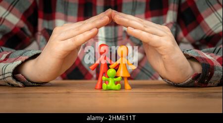 Young Family Insurance Concept mit bunten Familienfiguren, die mit Händen auf einem Holztisch bedeckt sind. Sicherheit und Unterstützung Stockfoto