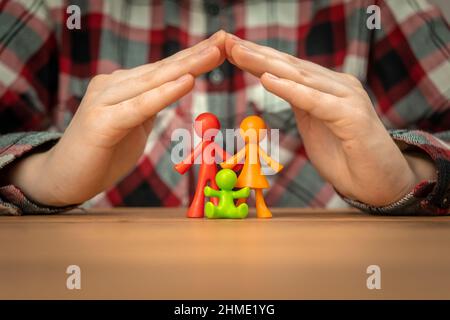 Young Family Insurance Concept mit bunten Familienfiguren, die mit Händen auf einem Holztisch bedeckt sind. Sicherheit und Unterstützung Stockfoto