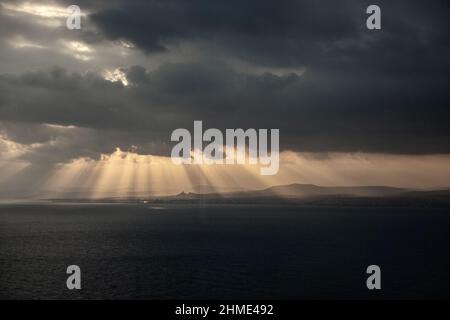 Wunderschöne Lichtstrahlen, die durch Sturmwolken über die Landschaftslandschaft mit dem Meer im Vordergrund strömen Stockfoto