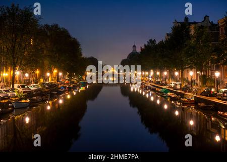 Niederlande. Nacht Amsterdam. Laternen und geparkte Autos auf den Böschungen. Viele Boote liegen an den Ufern des Kanals Stockfoto