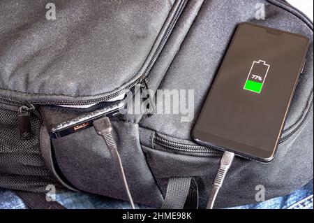 Das Smartphone wird von der daneben liegenden Powerbank in einem Rucksack aufgeladen. Modernes Technologiekonzept Stockfoto