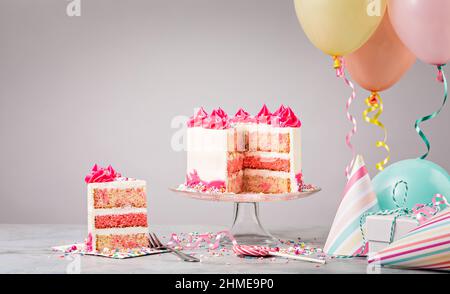 Geburtstagskuchen mit rosa Funfetti in Scheiben mit Geschenken, Hüten und bunten Luftballons auf hellgrauem Hintergrund. Szene von einer Geburtstagsfeier. Stockfoto