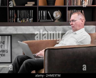 Der Geschäftsmann arbeitet online am Laptop und sitzt in einem Sessel in der Bürobibliothek. Hochwertige Fotos Stockfoto