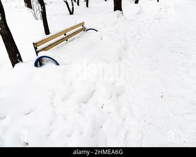 Schneebedeckte Bank in der Nähe von Pfad im Schnee im Stadtgarten an bewölkten Wintertag getreten Stockfoto