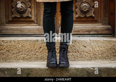 Angesagter schwarzer Stiefelette. Modischer Lederschuh aus nächster Nähe. Weibliche Beine stehen auf der Treppe auf der Straße Stockfoto