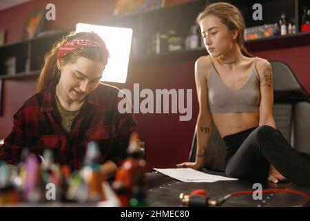 Attraktive weibliche sitzen im Tattoo-Salon neben Tattoo-Meister Stockfoto