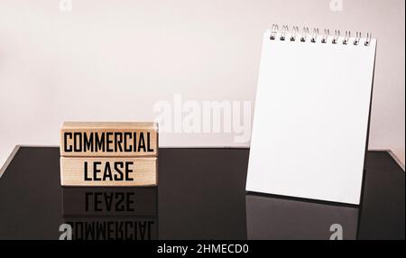 Geschäftskonzept. Draufsicht auf den Desktop mit Holzblöcken und Text, Commercial Lease. Neben einem Notizblock zum Schreiben auf weißem und schwarzem Hintergrund Stockfoto