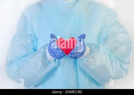 Eine Ärztin in einem Schutzanzug hält ein rotes Herz in ihren Händen in Handschuhen auf weißem Hintergrund Stockfoto