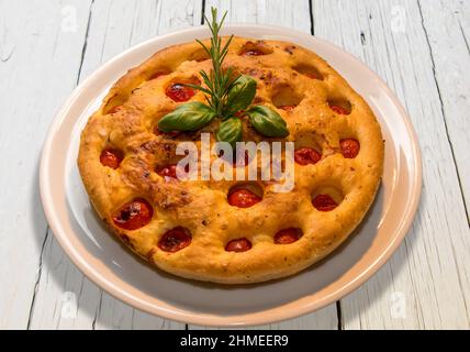 Apulian Focaccia, typisch italienische Pizza aus Bari mit einem Teig aus Hartweizenmehl und Kartoffeln mit Kirschtomaten darauf. In weißer Platte auf weiß Stockfoto