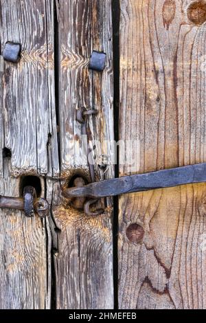 Altes Blockhaus. Türen, Tore. Geschmiedete Türgriffe aus rostetem Metall, Schrauben, Scharniere, Haken. Schäbiger Baum, gealterte Holzstruktur. Stockfoto