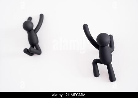 2 schwarze 3D Marionetten, die über einen weißen Hintergrund klettern, menschlicher Charakter, Person, die an einer weißen Wand hängt, eine versucht, der anderen zu helfen, die aus f ist Stockfoto
