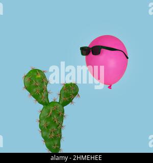 Kaktuspflanze, über der ein rosa Ballon in Sonnenbrillen schwimmt, isoliert auf einem pastellblauen Hintergrund. Kreatives Minimalkonzept. Für Karte, Poster verwenden Stockfoto