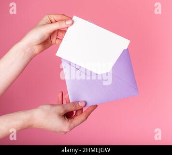 Hände mit leerer Grußkarte im Umschlag. Valentinstag-Konzept. Liebesbrief oder Urlaubseinladung mockup. Frau legt Karte in den Umschlag. Hochwertige Fotos Stockfoto