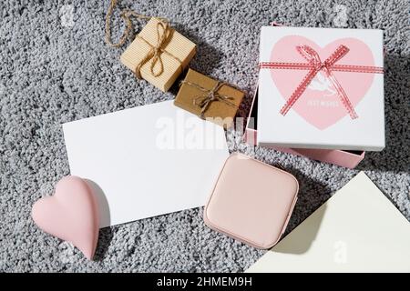 Grußkarte zum Valentinstag. Umschläge, eingewickelte Schachteln, Keramik rosa Herz auf einem grauen flauschigen Teppich Hintergrund. Speicherplatz kopieren. Für Text platzieren Stockfoto