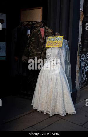 "Spenden erforderlich"-Schild auf einer Schaufensterpuppe in einem weißen Kleid vor einem Shelter Charity Shop in Forrest Road, Edinburgh, Schottland, Großbritannien. Stockfoto