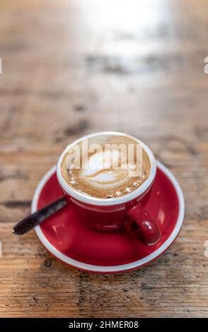 Von oben Tasse frischen Latte mit Schaum Herz auf Untertasse mit Löffel auf Holztisch im Café gelegt Stockfoto
