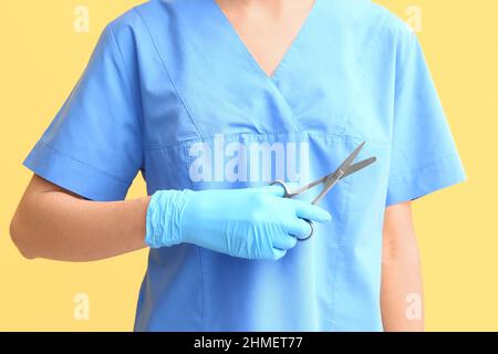 Ärztin mit medizinischer Schere auf gelbem Hintergrund, Nahaufnahme Stockfoto