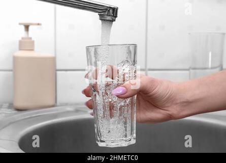 Frau, die im Badezimmer Glas mit Wasser aus dem Wasserhahn füllte, Nahaufnahme Stockfoto