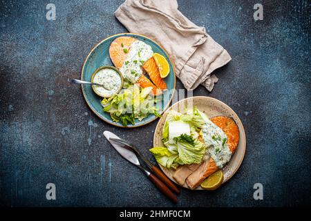 Gesundes Essen gegrillte Lachssteaks mit Dillsauce und Salatblättern auf zwei Tellern Stockfoto