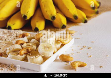 Banane, Cashewnüsse und Flocked Hafer. Natürliche Lebensmittel. Hintergrund mit Bananen im Bund. Stockfoto