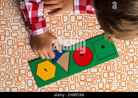 Das Kind sammelt den Sortierer-Konstruktor. Puzzle Sorter, ein frühes Entwicklungskonzept. Die Hände der Kinder legen das Puzzle auf den Tisch. Spielen Sie Kurse für Stockfoto