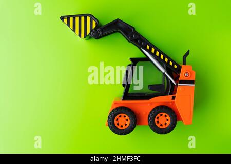 Orange Toy Loader auf grünem Hintergrund, Mini-Lader, Toy Industrial Car, Kunststoff-Vorderradlader. Stockfoto